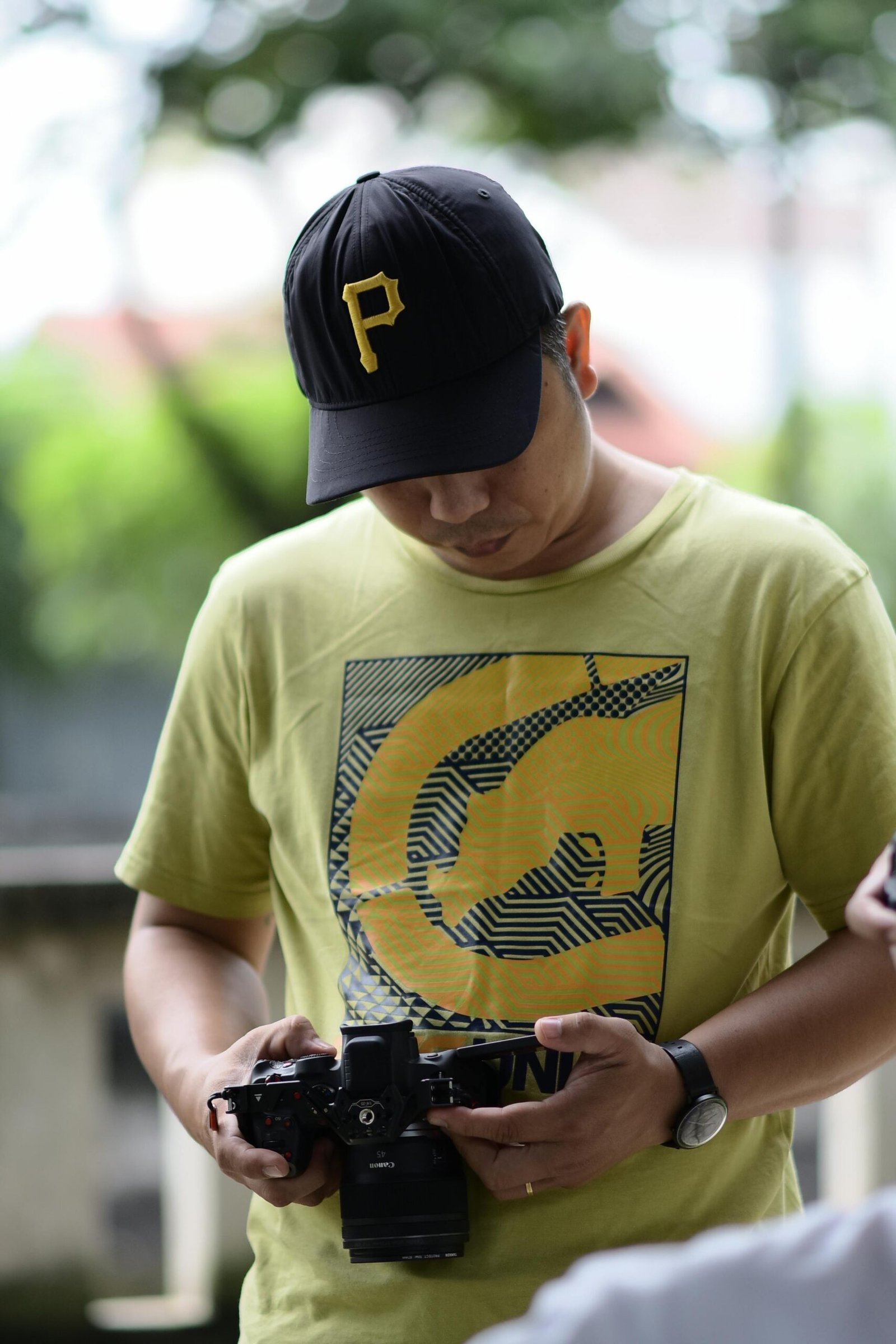 A man in a cap focusing on adjusting his camera outside. Natural daylight setting.